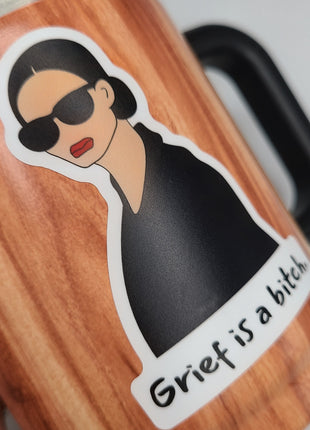 Close up of high quality dishwasher safe sticker on mug. "Grief is a bitch" by Deathday Cards