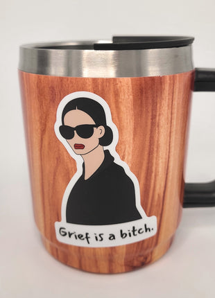 Grief is a bitch sticker on woodgrain mug. Empowering sticker by Deathday Cards