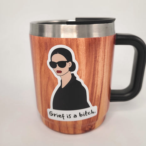 Grief is a bitch sticker on woodgrain mug. Empowering sticker by Deathday Cards