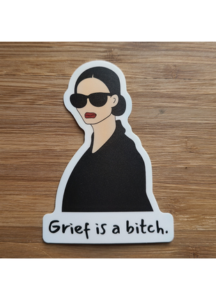 Chic woman in shades above the words "Grief is a bitch". Snarky sticker by Deathday Cards
